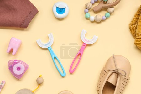 Téléchargez les photos : Vêtements pour bébés avec brosses à dents, fil dentaire et jouets sur fond beige - en image libre de droit