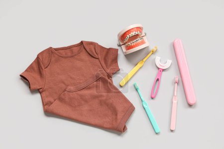 Téléchargez les photos : Vêtements bébé avec brosses à dents, étui et modèle à mâchoires sur fond blanc - en image libre de droit