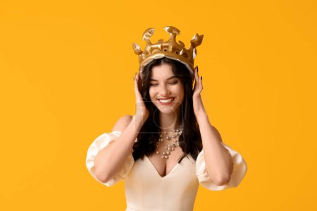 Hermosa mujer joven en vestido de fiesta elegante y corona inflable sobre fondo amarillo