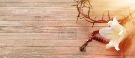 Crown of thorns, rosary beads and white lily on wooden background with space for text