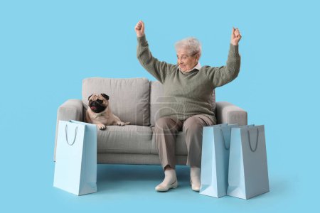 Happy senior woman with shopping bags and pug dog sitting on sofa against blue background
