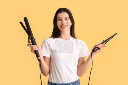 Téléchargez les photos : Belle jeune femme heureuse avec des fers à friser sur fond jaune - en image libre de droit