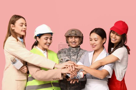 Mujeres de diferentes profesiones poniendo las manos juntas sobre fondo rosa