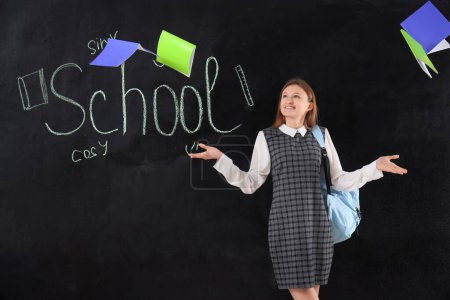 Photo for Female student throwing copybooks away near word SCHOOL written on blackboard. End of school concept - Royalty Free Image