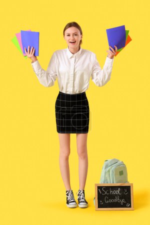 Photo for Female student with copybooks and chalkboard with text GOODBYE SCHOOL on yellow background. End of school concept - Royalty Free Image