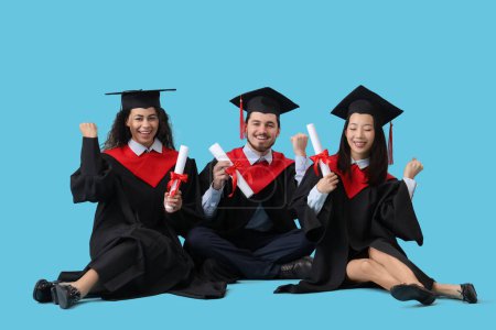 Photo for Graduate students with diplomas sitting on blue background - Royalty Free Image