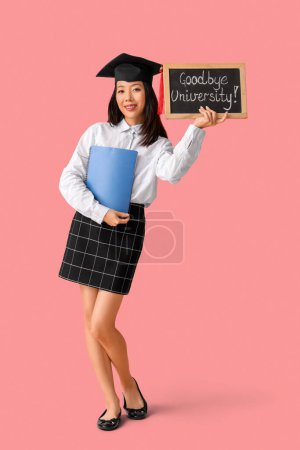 Photo for Asian female graduate student holding chalkboard with text GOODBYE UNIVERSITY on pink background - Royalty Free Image