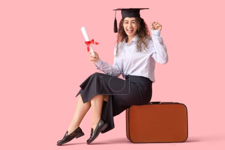 Photo for African-American female graduate student with diploma and suitcase on pink background - Royalty Free Image