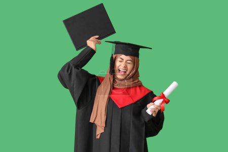 Photo for Muslim female graduate student with diploma throwing mortar board up on green background - Royalty Free Image
