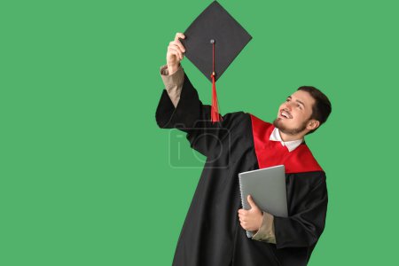 Photo for Male graduate student with notebook throwing mortar board up on green background - Royalty Free Image