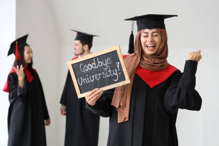 Photo for Muslim female graduate student holding chalkboard with text GOODBYE UNIVERSITY in light room - Royalty Free Image