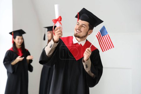 Photo for Male graduate student with diploma and USA flag in light room - Royalty Free Image
