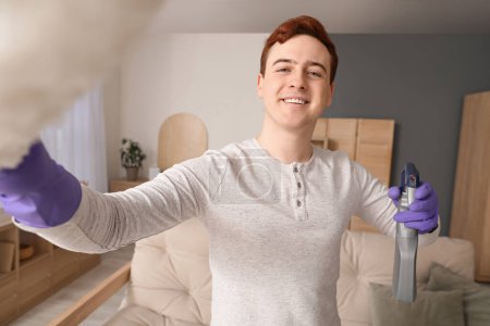 Junger Mann mit Staubwedel und Sprühflasche reinigt Wohnzimmer, Nahaufnahme