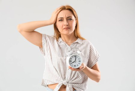 Mature woman with alarm clock on light background. Menopause concept