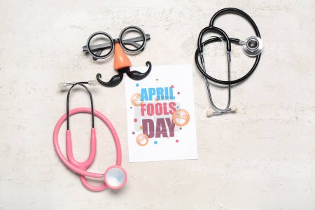 Photo for Card with text APRIL FOOL'S DAY, party decor and stethoscopes on light background - Royalty Free Image