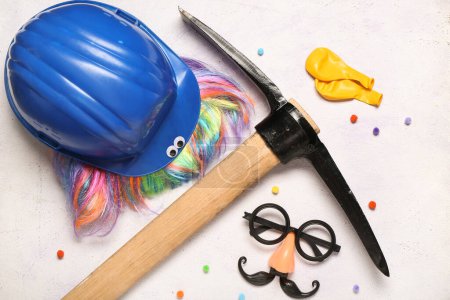 Composition with hardhat, pick and party decor on light background. April Fool's Day celebration
