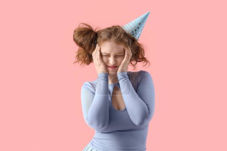 Mujer joven con resaca después de la fiesta de cumpleaños sobre fondo rosa