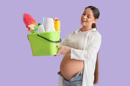 Junge schwangere Frau mit Putzmitteln auf fliederfarbenem Hintergrund