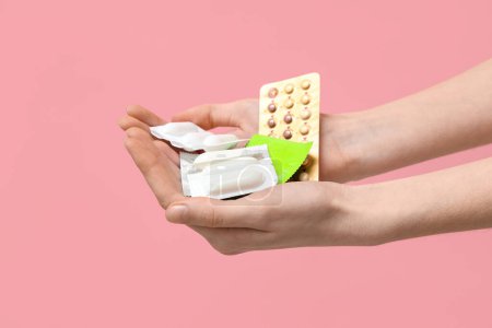 Female hands with birth control pills, vaginal suppositories and condoms on pink background