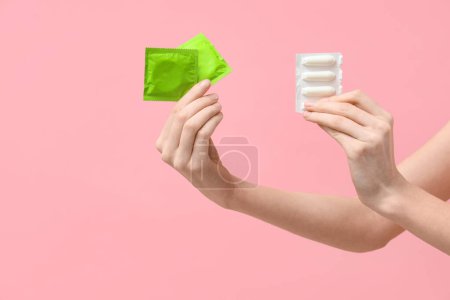 Female hands with condoms and vaginal suppositories on pink background