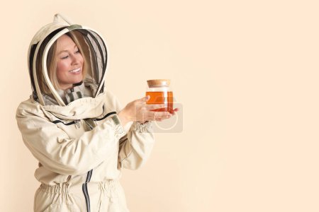 Female beekeeper with jar of sweet honey on beige background