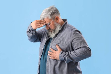 Photo for Elderly man having heart attack on blue background - Royalty Free Image