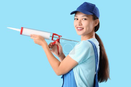 Téléchargez les photos : Femme asiatique plombier avec pistolet à calfeutrer sur fond bleu - en image libre de droit