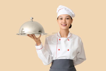 Téléchargez les photos : Femme chef asiatique avec cloche sur fond beige - en image libre de droit