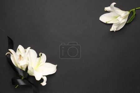Frame made of beautiful lily flowers with black funeral ribbon on dark background