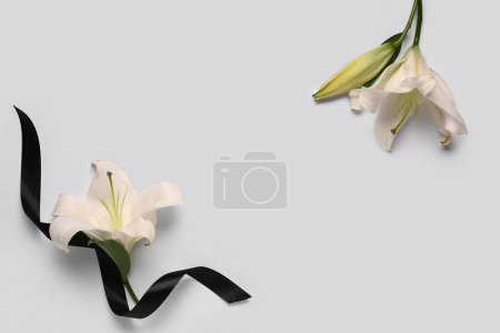 Frame made of beautiful lily flowers with black funeral ribbon on white background