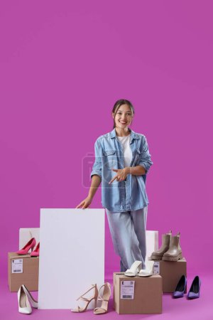 Photo for Young Asian seller with blank poster and shoes on purple background - Royalty Free Image