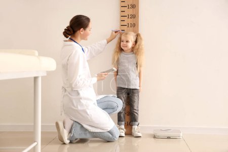 Kinderarzt misst Körpergröße von süßem kleinen Mädchen in der Nähe von Holzstadiometer in Klinik