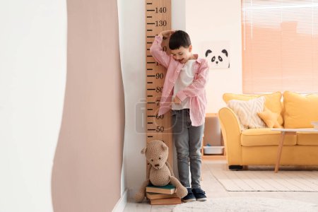 Cute little boy measuring height near wooden stadiometer at home
