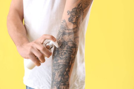 Hombre joven aplicando crema de tatuaje sobre fondo amarillo, primer plano