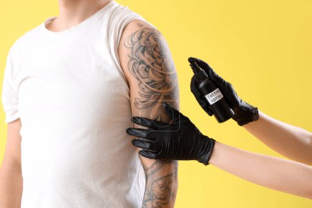 Tatuaje maestro pulverización brazo del hombre contra el fondo amarillo, primer plano