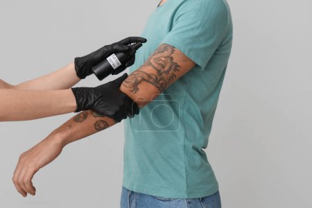 Tattoo master spraying man's arm on light background, closeup