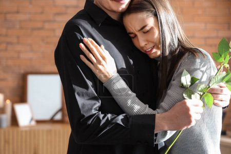 Mourning young couple with rose hugging at funeral