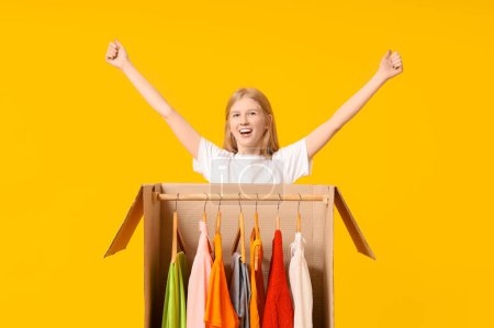 Foto de Hermosa mujer feliz joven y caja de armario con ropa sobre fondo amarillo - Imagen libre de derechos