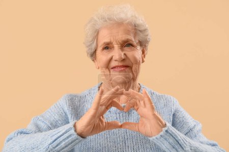 Femme âgée faisant coeur avec ses mains sur fond beige
