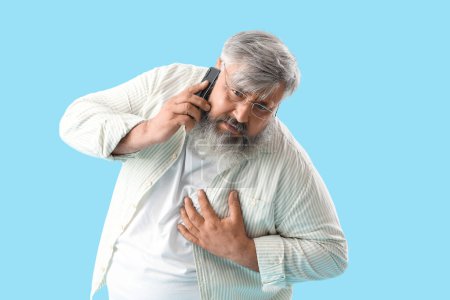 Photo for Middle-aged man with heart attack calling ambulance on blue background - Royalty Free Image