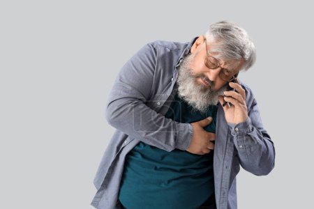 Photo for Middle-aged man with heart attack calling ambulance on grey background - Royalty Free Image
