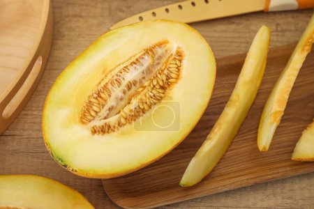 Board with cut fresh melon and knife on brown wooden background