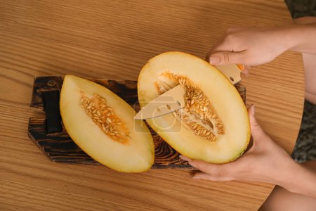 Frau schneidet frische Melone auf braunem Holzhintergrund