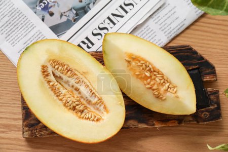 Brett mit geschnittener frischer Melone und Zeitung auf braunem Holzgrund