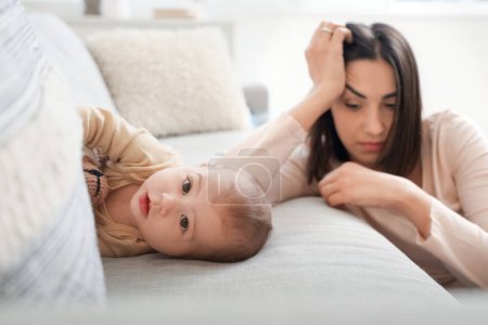 Kleines Baby auf dem Sofa und junge Frau, die zu Hause an postnataler Depression leidet, Nahaufnahme