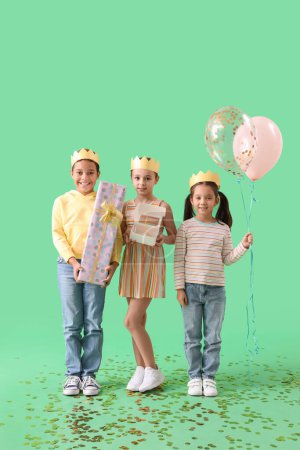 Photo for Cute little children in crowns with Birthday gift, cake and balloons on green background - Royalty Free Image