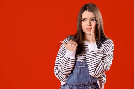 Photo for Gossiping young woman pointing at something on red background. Accusation concept - Royalty Free Image