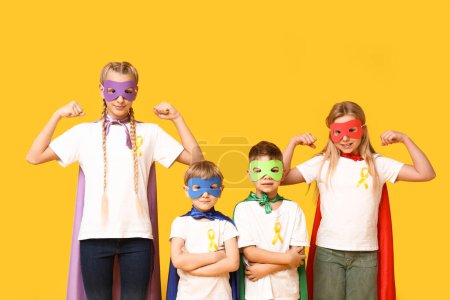 Téléchargez les photos : Groupe d'enfants en costumes de super-héros avec des rubans jaunes sur fond de couleur. Journée internationale du cancer chez les enfants - en image libre de droit