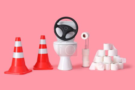 Toilettenschüssel mit Lenkrad, Verkehrskegeln und Papierrollen auf rosa Hintergrund