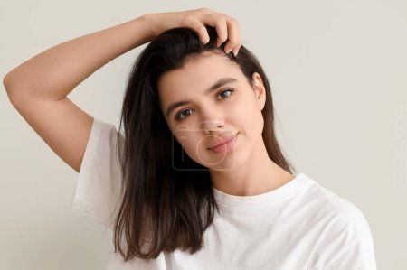 Young woman with dandruff problem examining her hair on white background